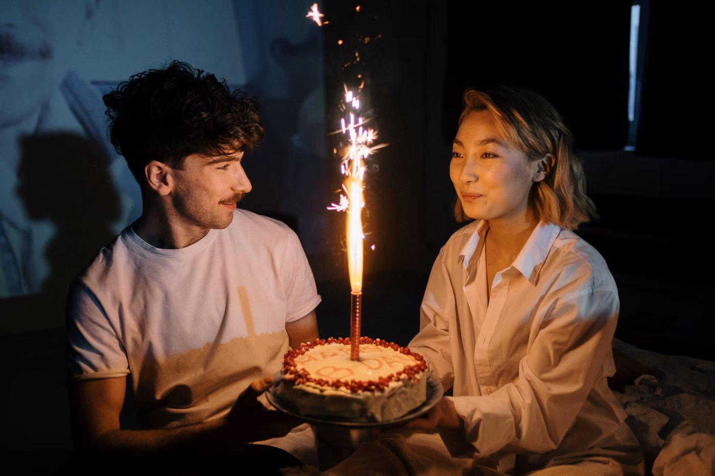 A couple holding a birthday cake together as a sparkler glows