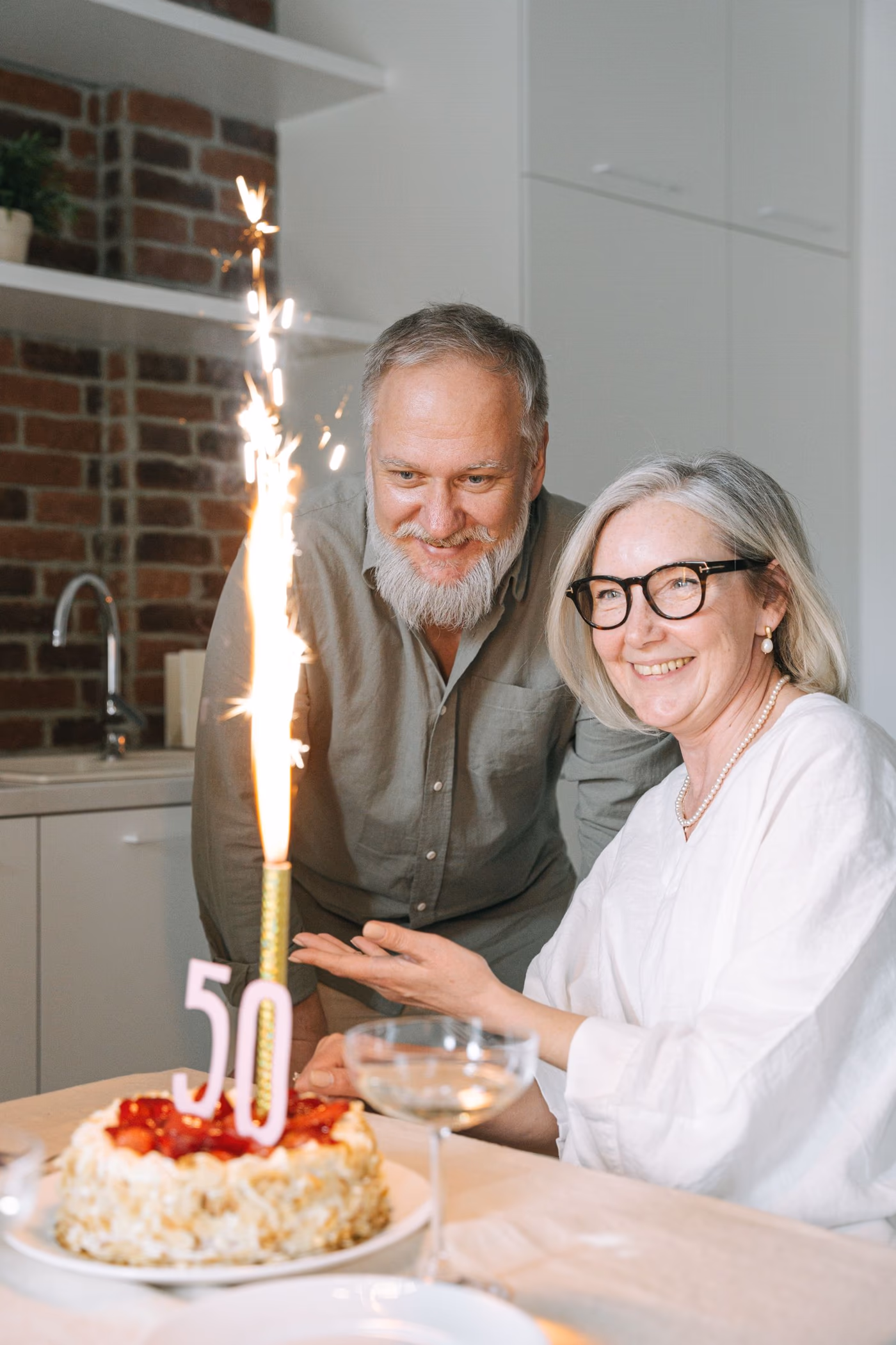 An older couple smiling beside a sparkler-lit 50th birthday cake
